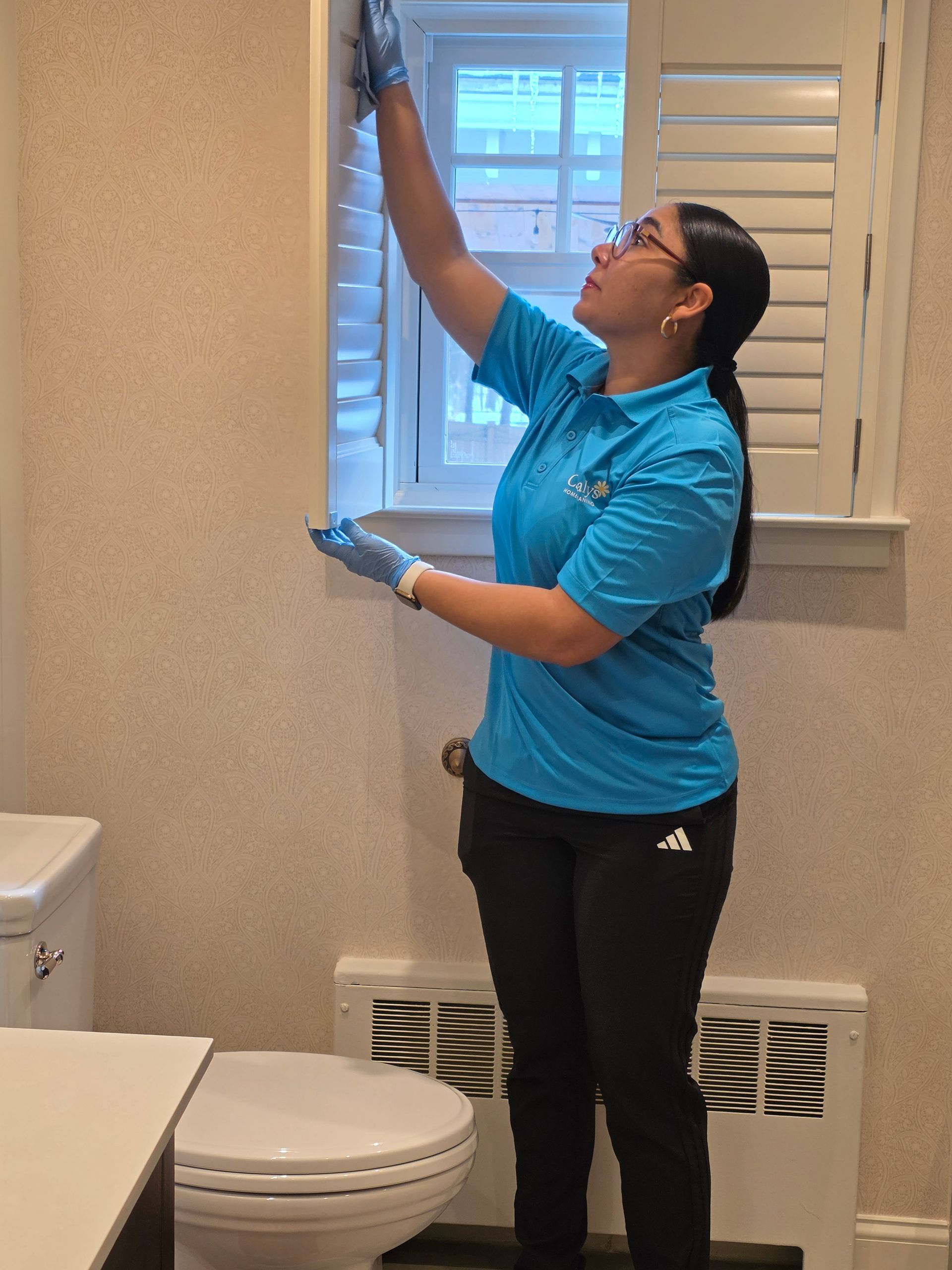Person cleaning a bathroom window with a squeegee, wearing blue shirt and black pants.