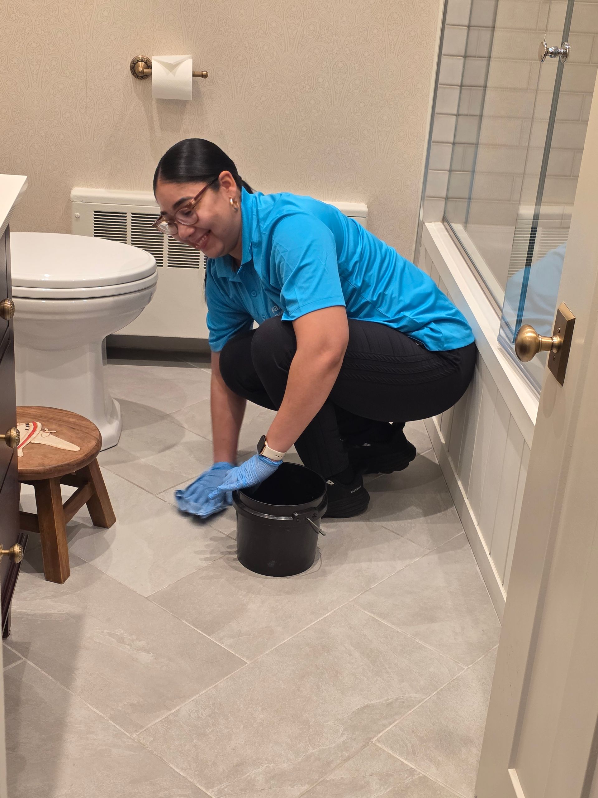 Person in a blue shirt cleaning a bathroom floor beside a toilet and bathtub.