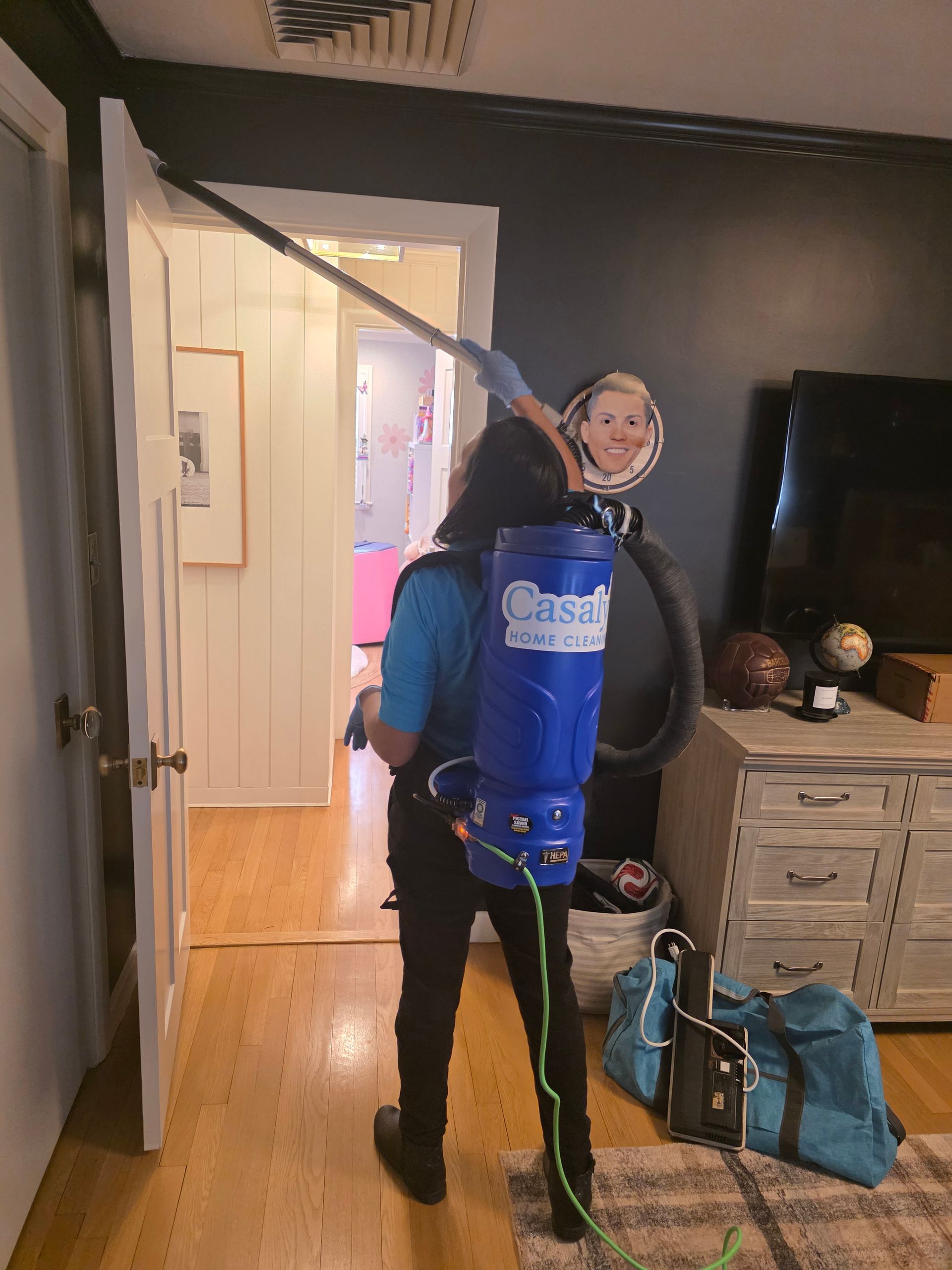 Person in blue vacuum backpack stands in a doorway holding the hose in a living room.