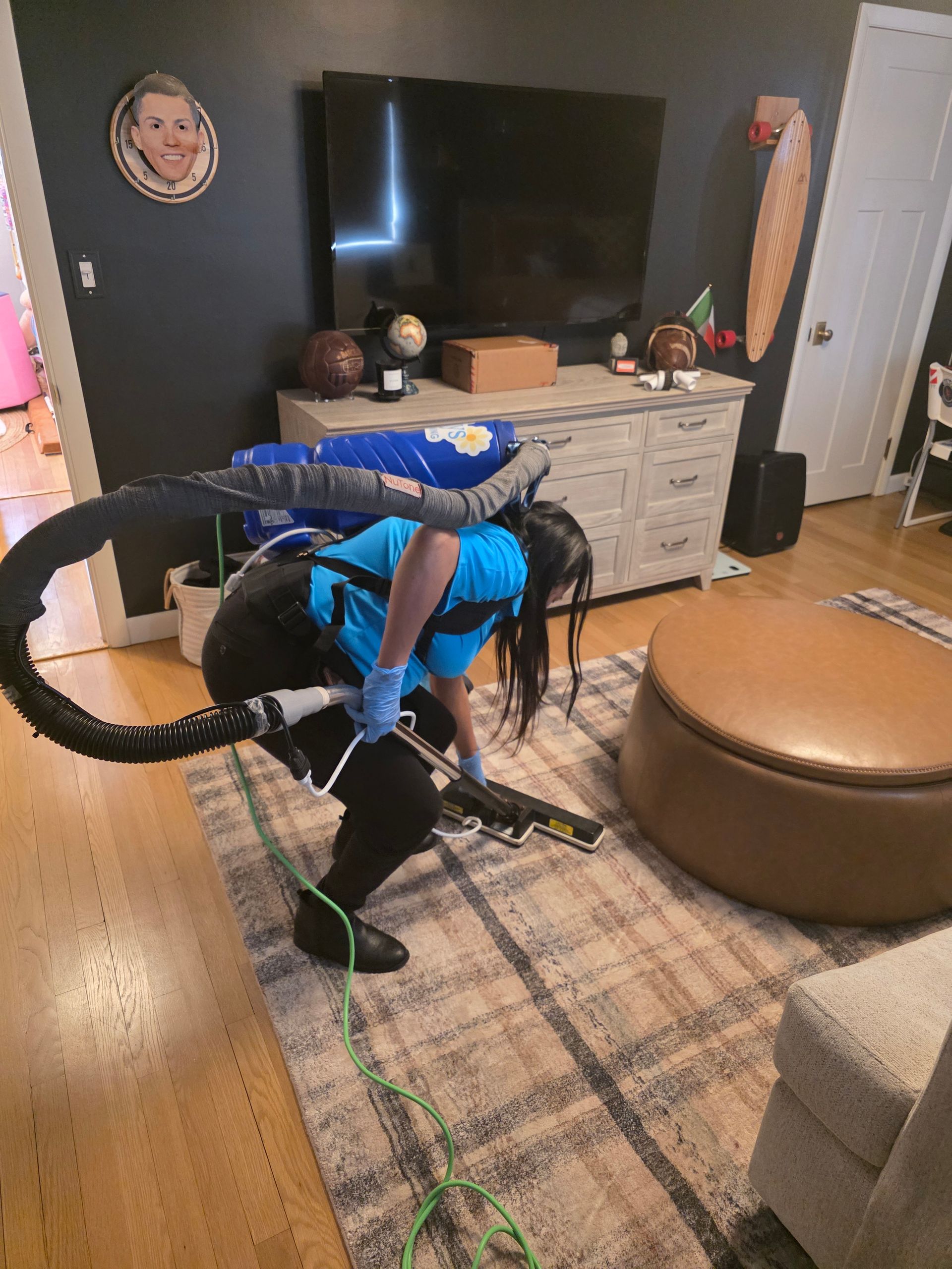 Person in a blue costume posing in a living room beside a TV, dresser, and round ottoman.