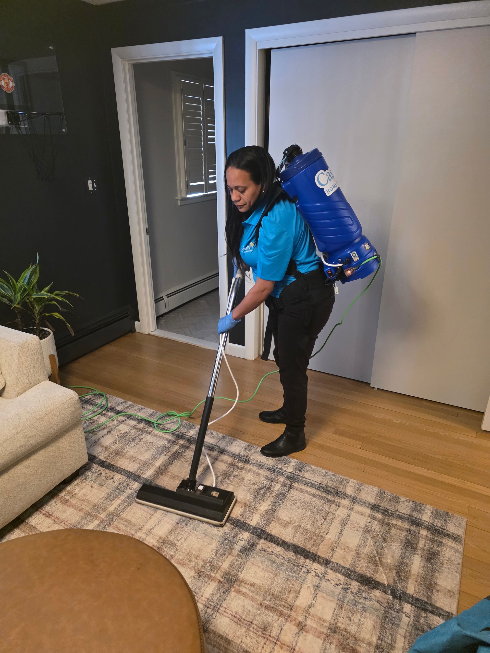 Person vacuuming a rug in a living room, wearing a blue backpack vacuum.