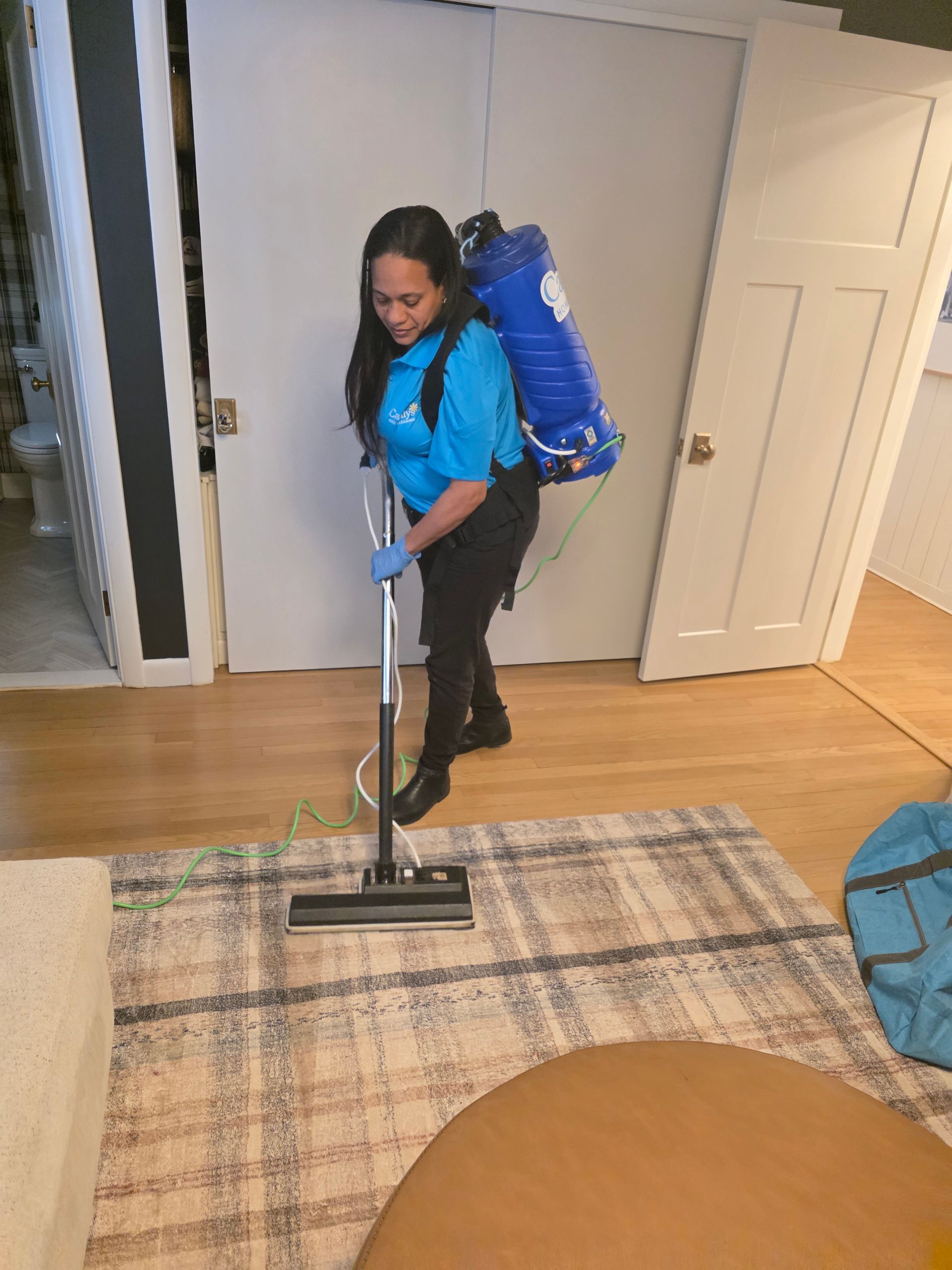Person vacuuming a rug in a living room while wearing a blue backpack vacuum.