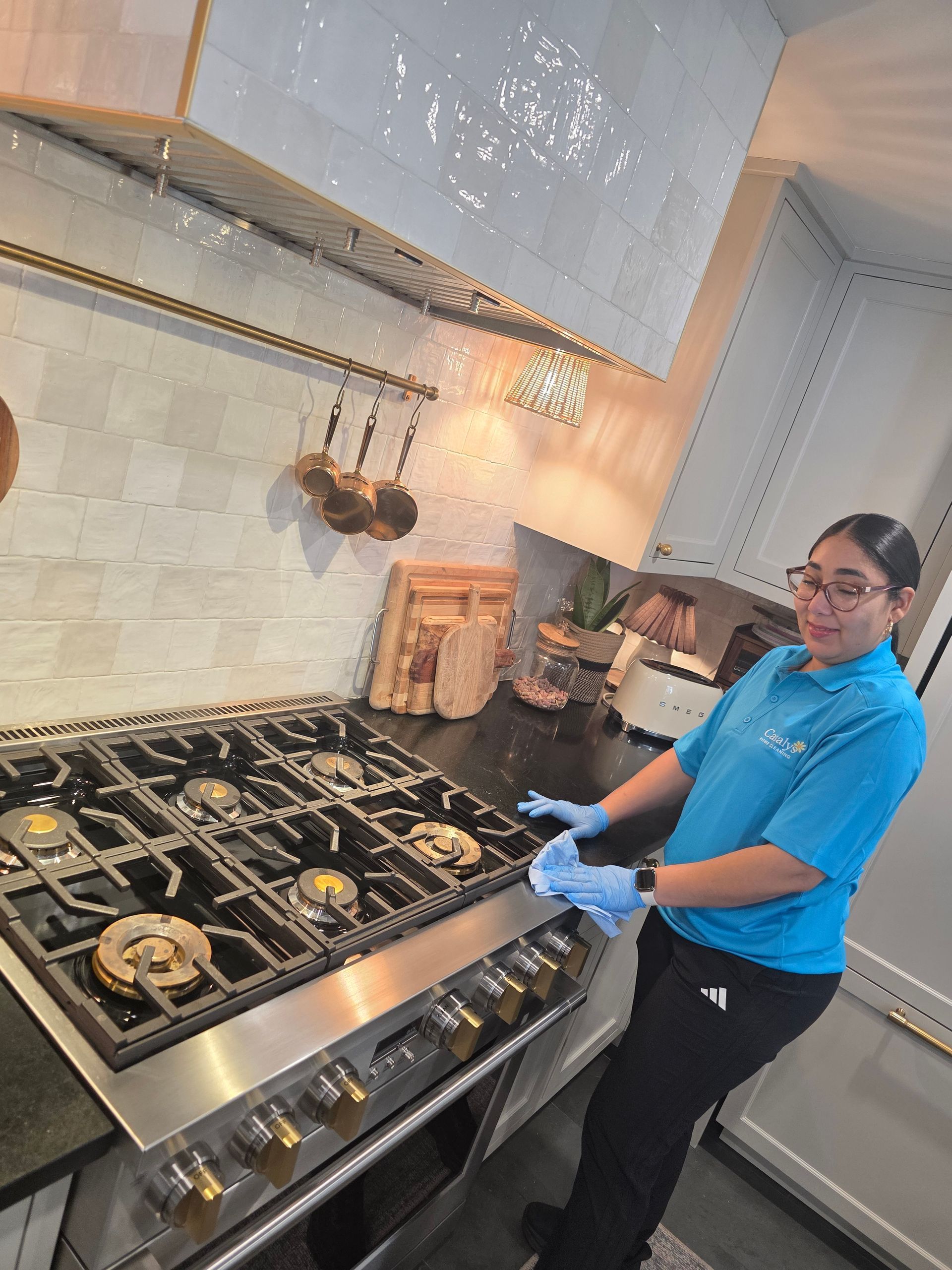 Person in blue shirt and gloves standing beside a gas stove in a modern kitchen.