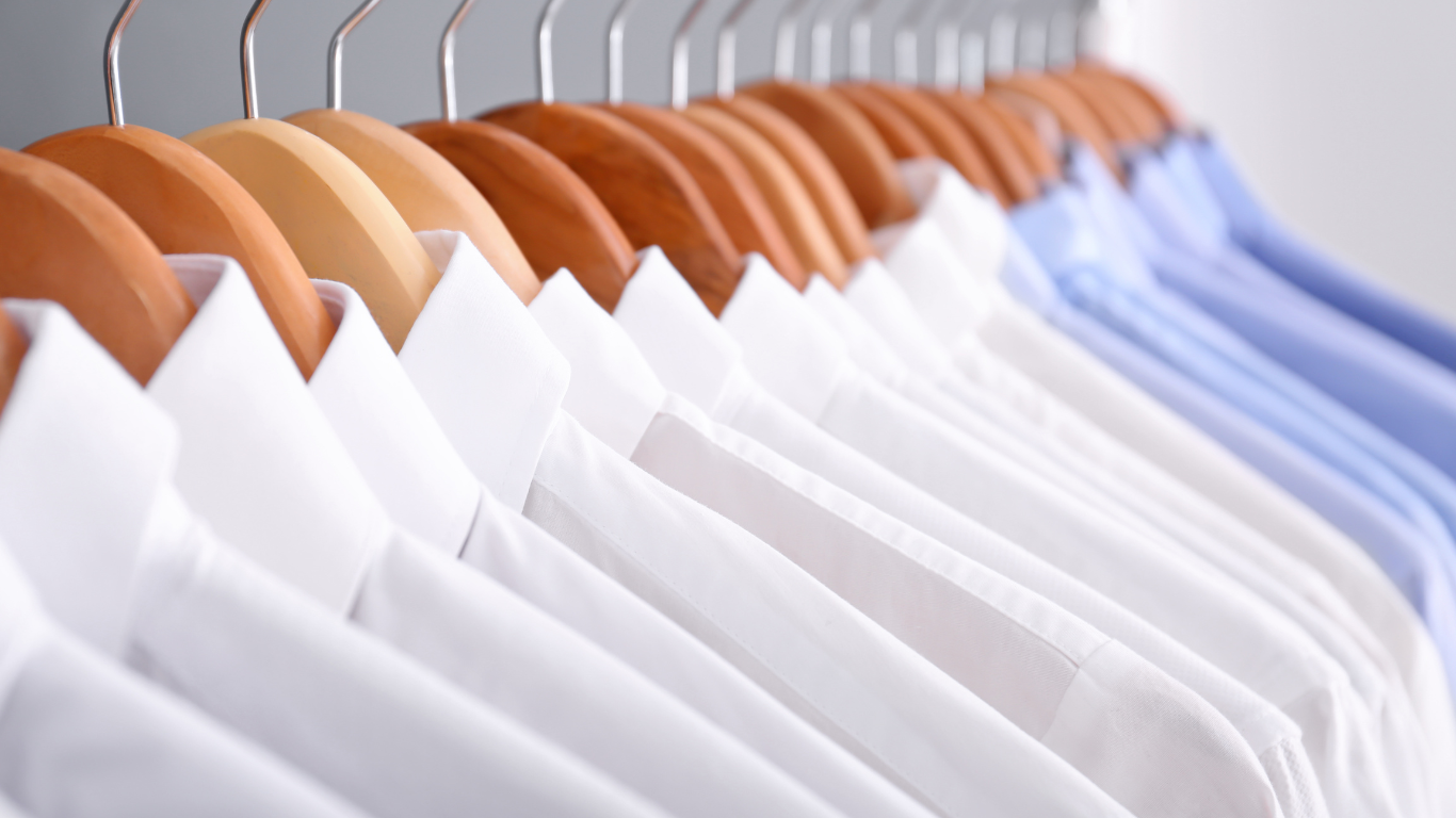 Row of white and blue button-down shirts hanging on wooden hangers.