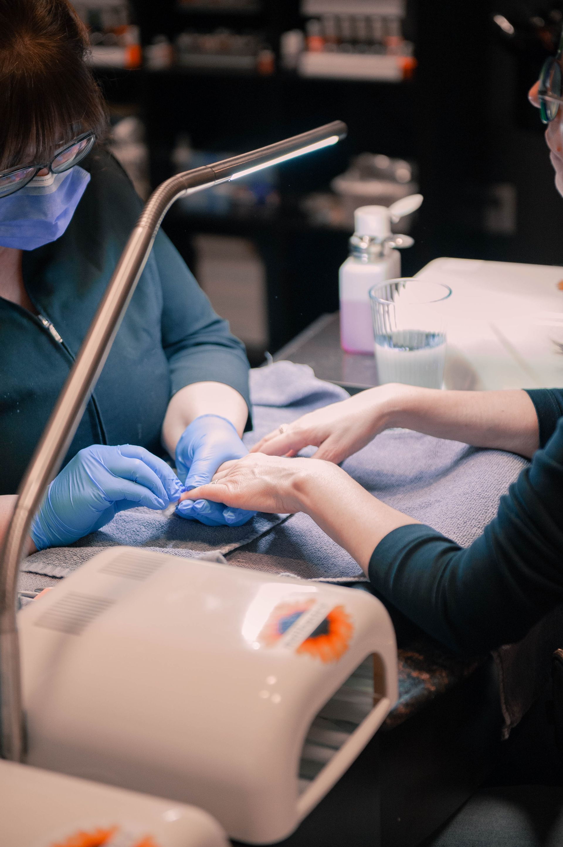 A woman is getting her nails painted by a nail artist wearing black gloves.