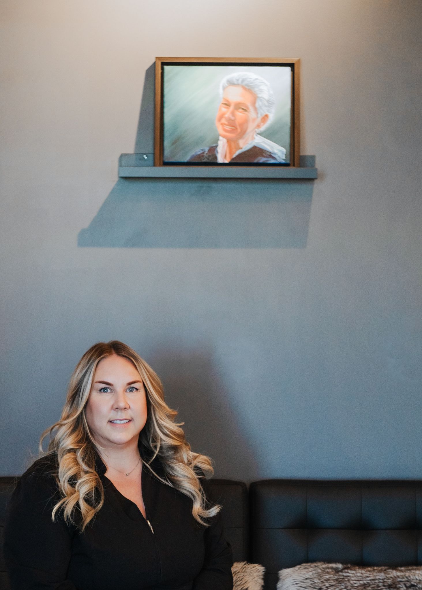 A woman is sitting on a couch in front of a painting on a wall.