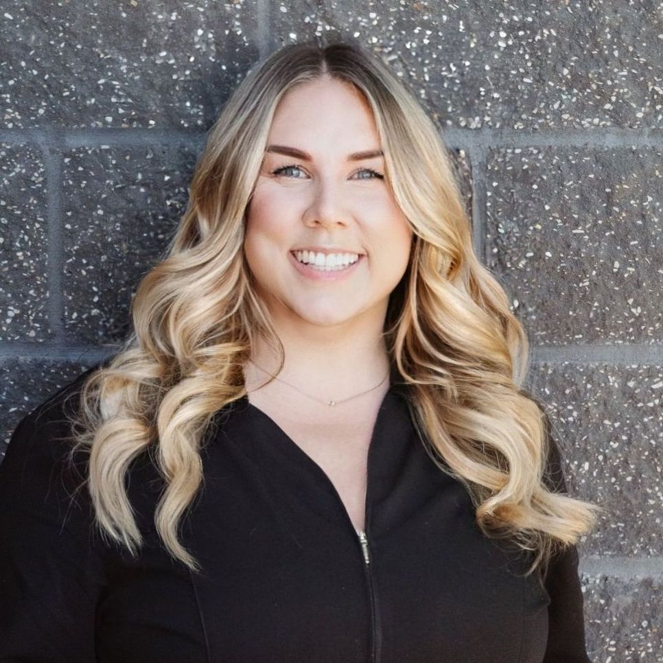 A woman with blonde hair is smiling in front of a brick wall.