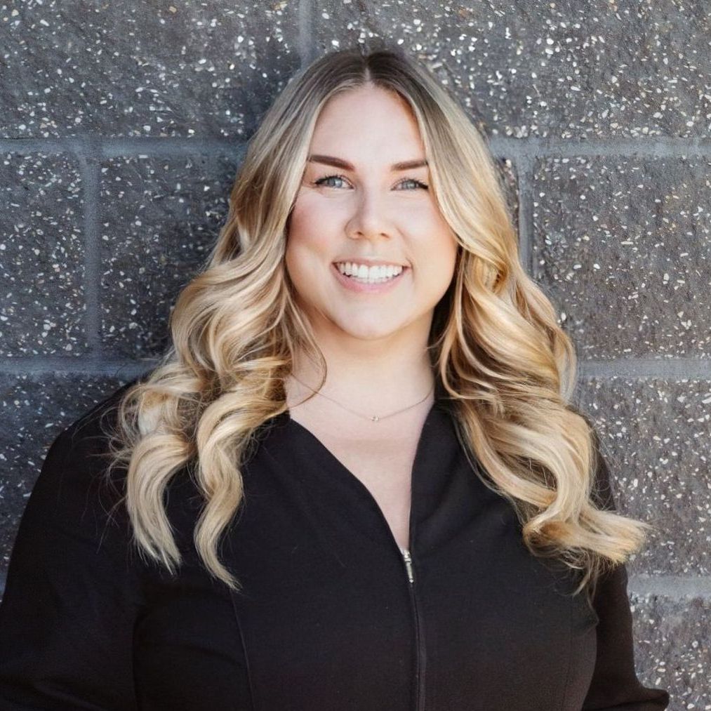 A woman with blonde hair is smiling in front of a brick wall