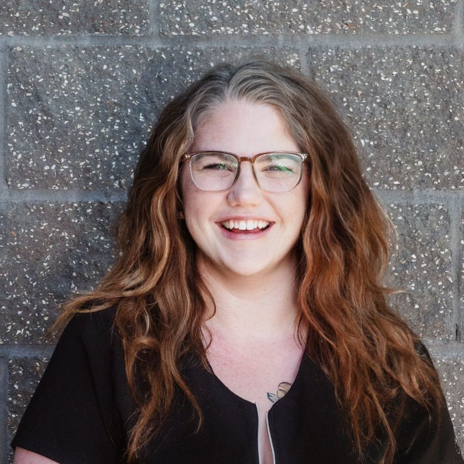 A woman in a black shirt is smiling in front of a brick wall.