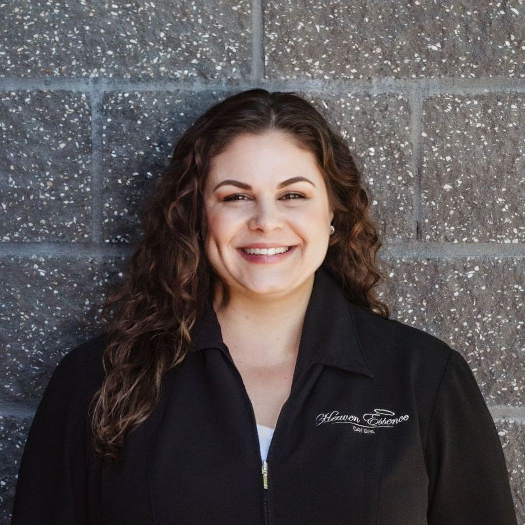 A woman in a black jacket is smiling in front of a brick wall.