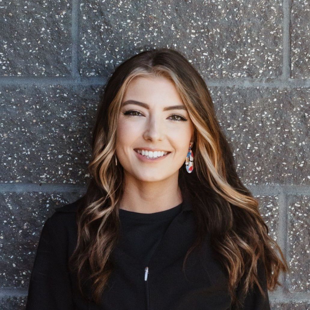 A woman in a black shirt and earrings is smiling in front of a brick wall.