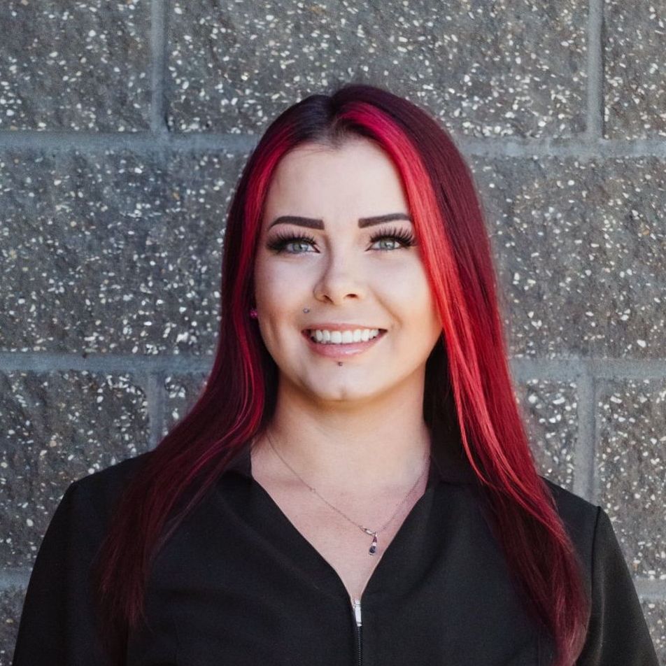 A woman in a black shirt and earrings is smiling in front of a brick wall.