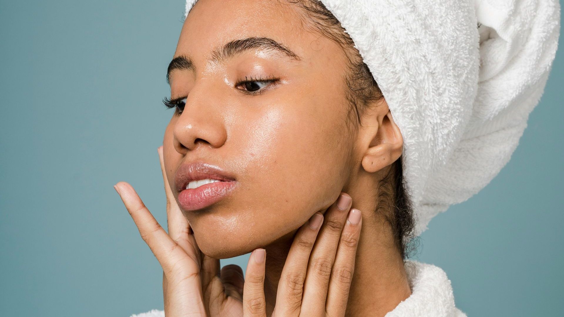A woman with a towel wrapped around her head is looking at her face.