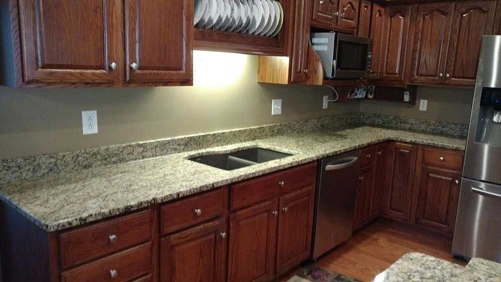 Granite kitchen countertops with dark wood cabinets and stainless steel appliances in a corner layout