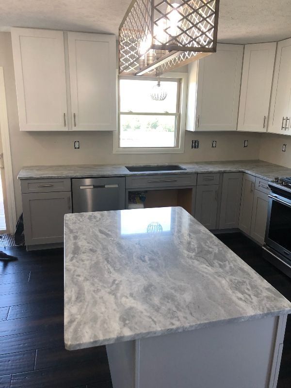 Bright kitchen with white cabinets, gray island countertop, stainless dishwasher, and a window over the sink.