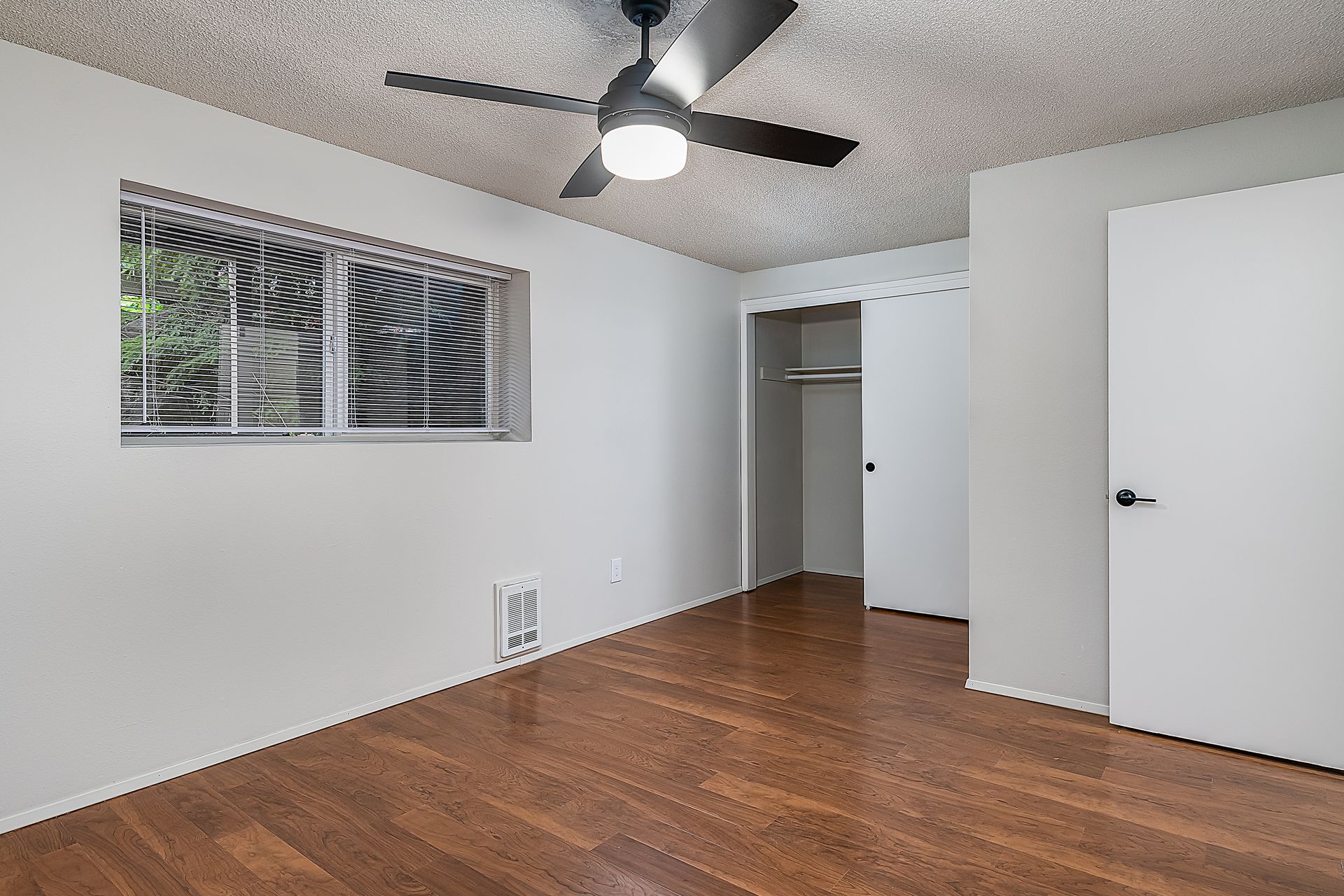 Photo showing a bedroom with a ceiling fan and sliding closet doors, from an alternate angle