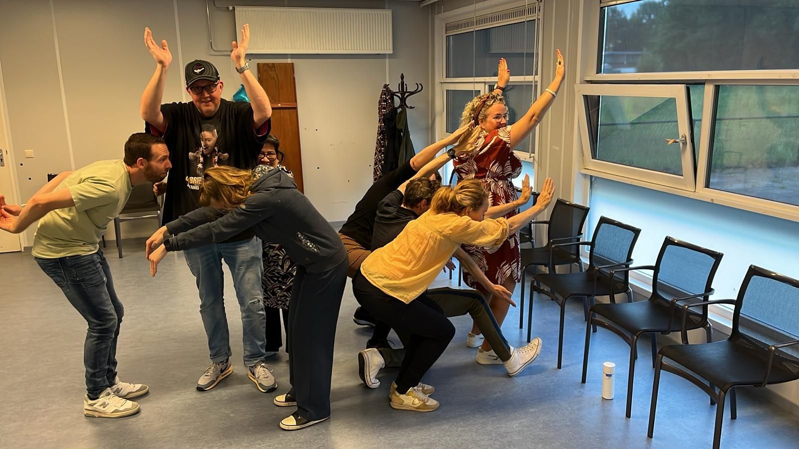 Een groep mensen poseert. Sommigen hebben hun armen omhoog, anderen staan ​​voorovergebogen. 