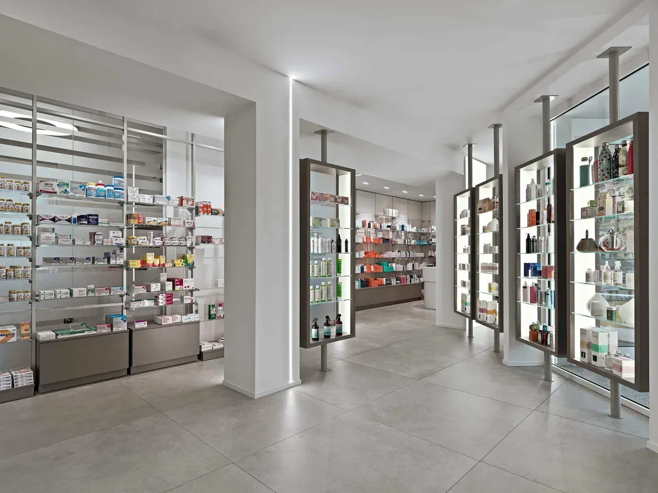 Arredamento Farmacia Passirani Lesa, expo a parete con tubolari fissaggio pavimento e soffitto, cassettoni con apertura push-pull
