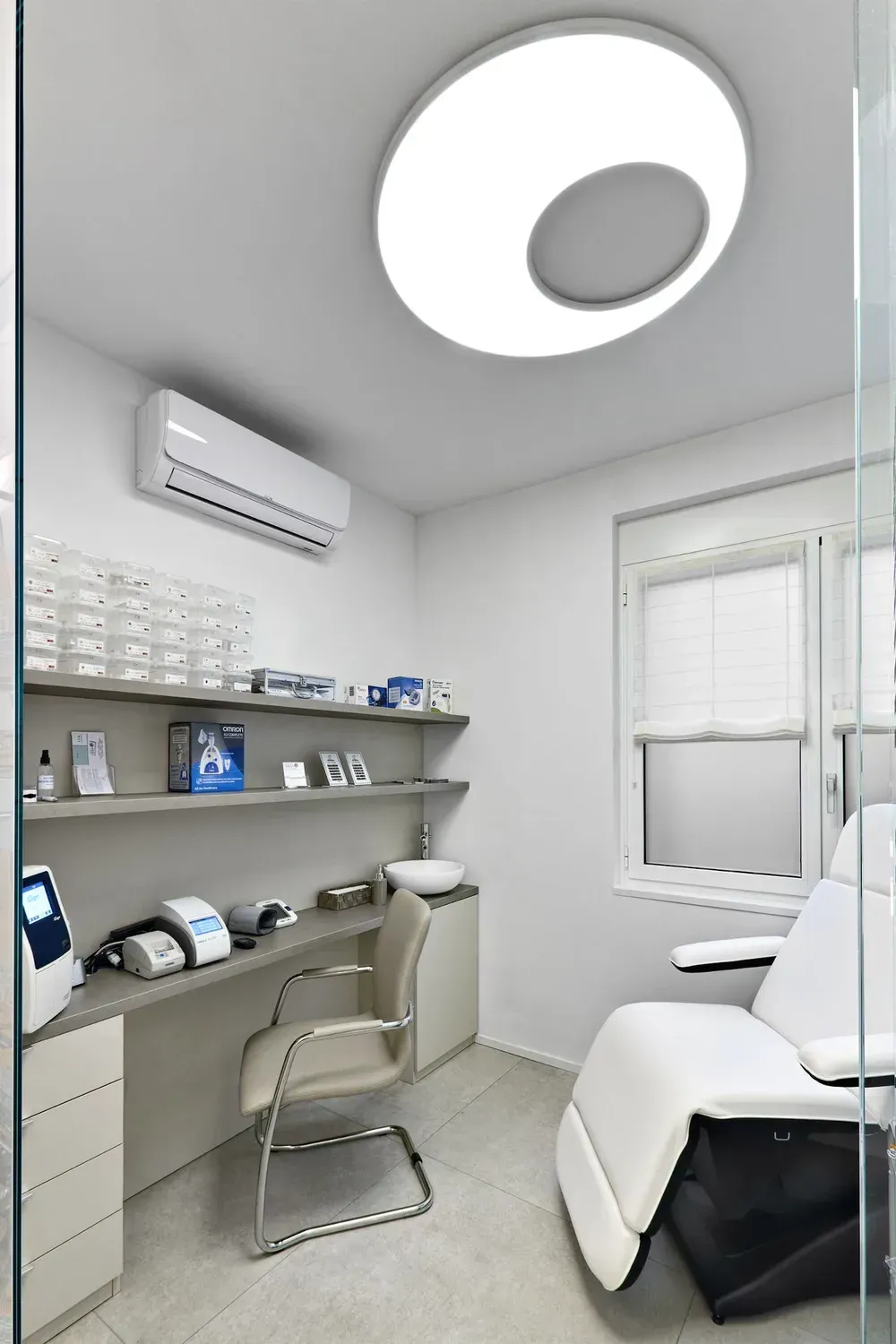 Arredamento Farmacia Passirani Lesa, cabina polifunzionale, lettino, piano con cassettiera, pannello salvamuro con ripiani e lampada Elcom