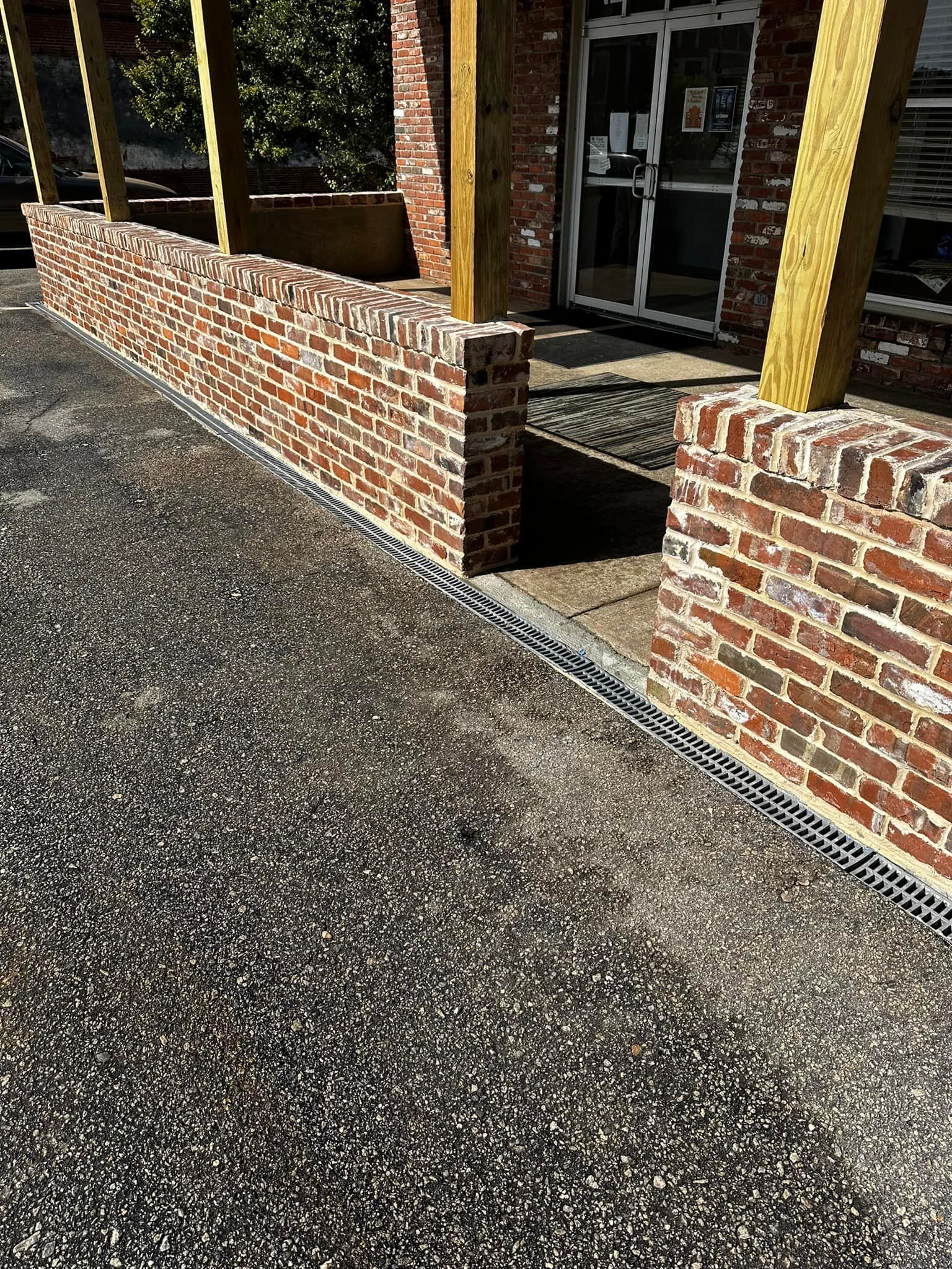 Brick wall borders asphalt walkway leading to a building with glass doors.