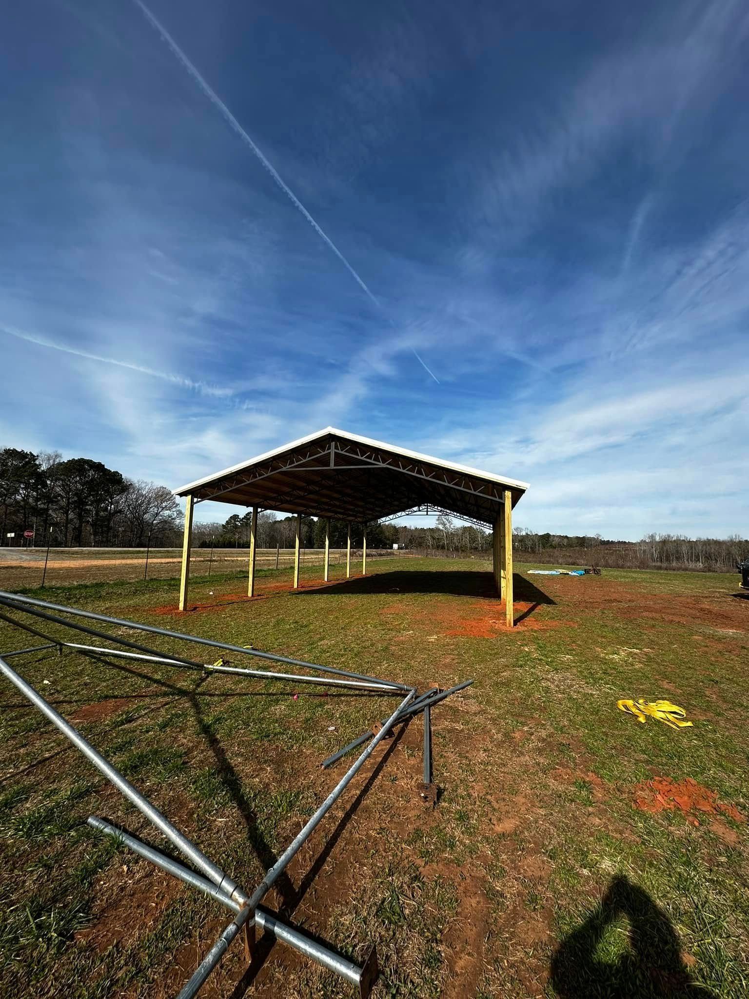 A partially-built metal-roofed shelter in a grassy field under a blue sky.