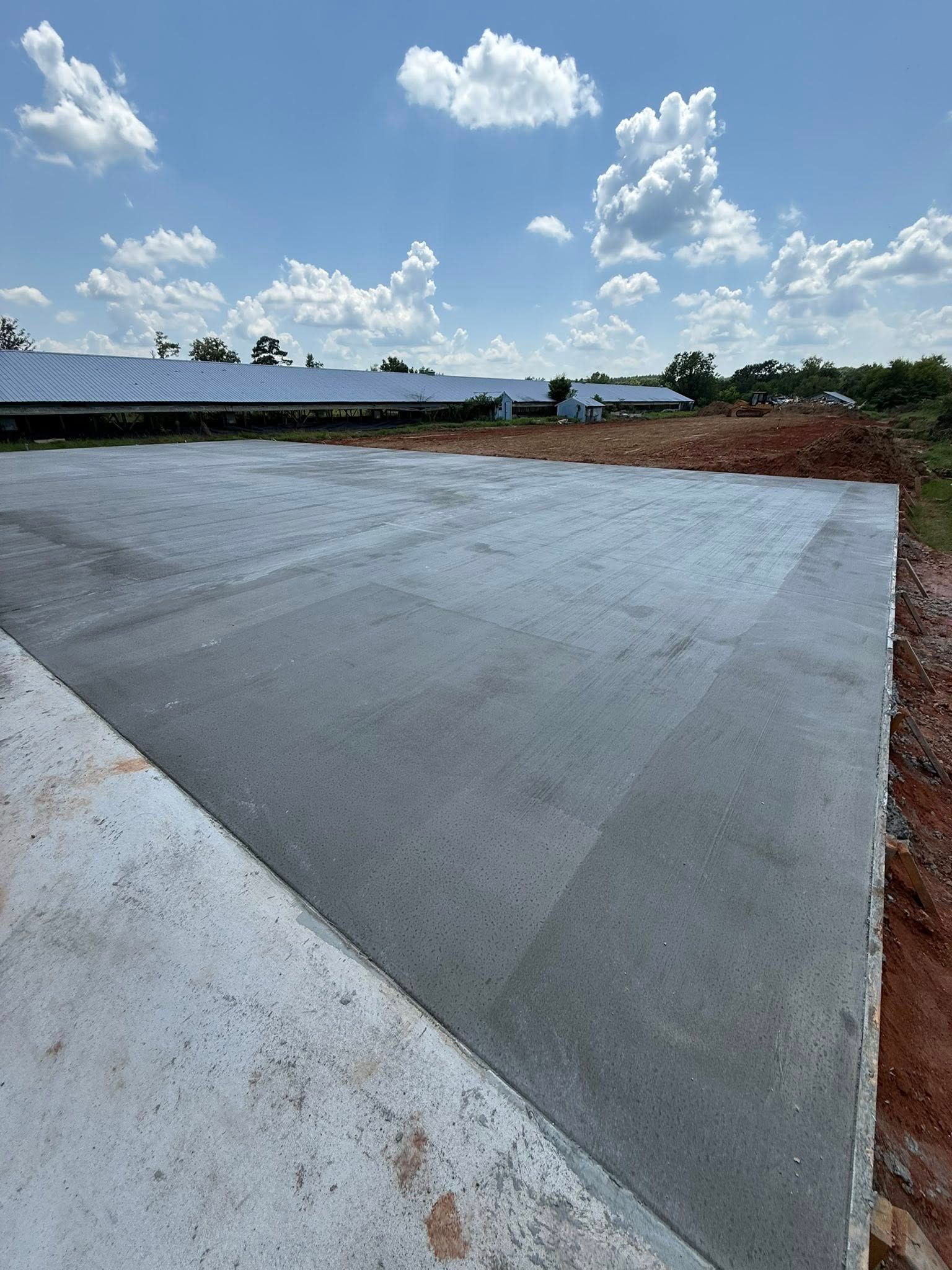 Concrete slab in a sunny outdoor setting with blue sky and clouds, construction site.