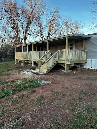 Newly constructed wooden deck with stairs and roof attached to a house, in a yard.