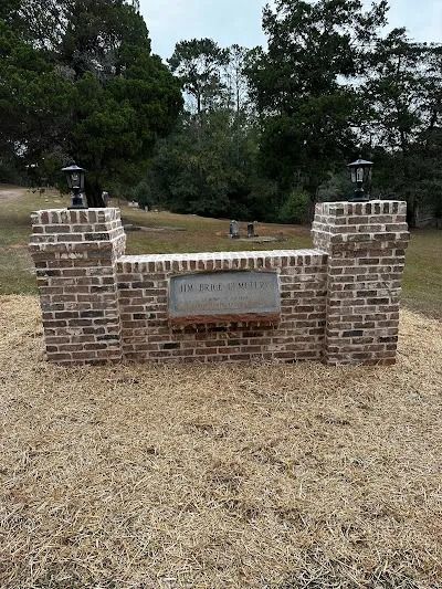 Brick entrance with a plaque and lanterns, set in a grassy area with trees in the background.