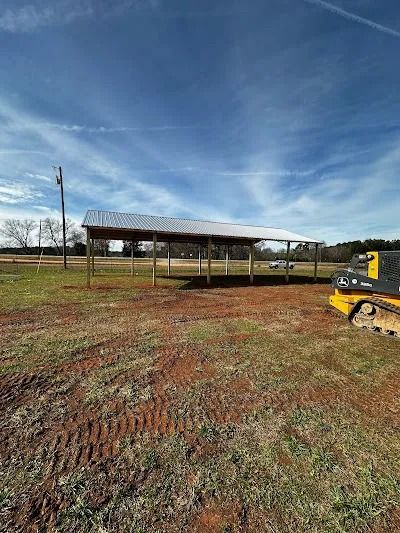 A metal-roofed shelter on wooden posts in a field, with a small tractor to the right.