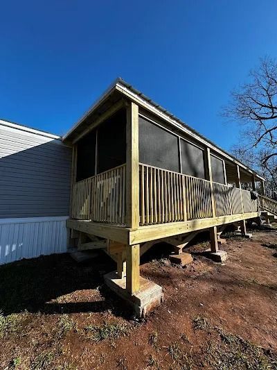 Screened-in porch attached to a house with wooden railings and support posts, set against a blue sky.