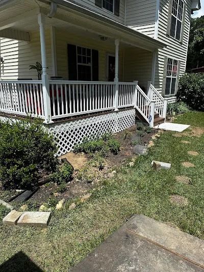 Yellow house with white porch and lattice, front yard with grass, stone pavers, and plants.