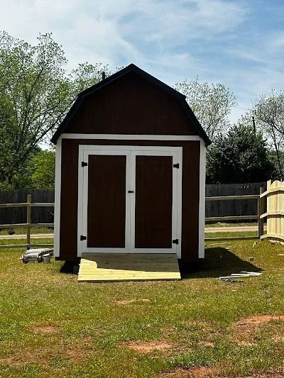 Brown shed with white trim, double doors, and wooden ramp on green lawn.