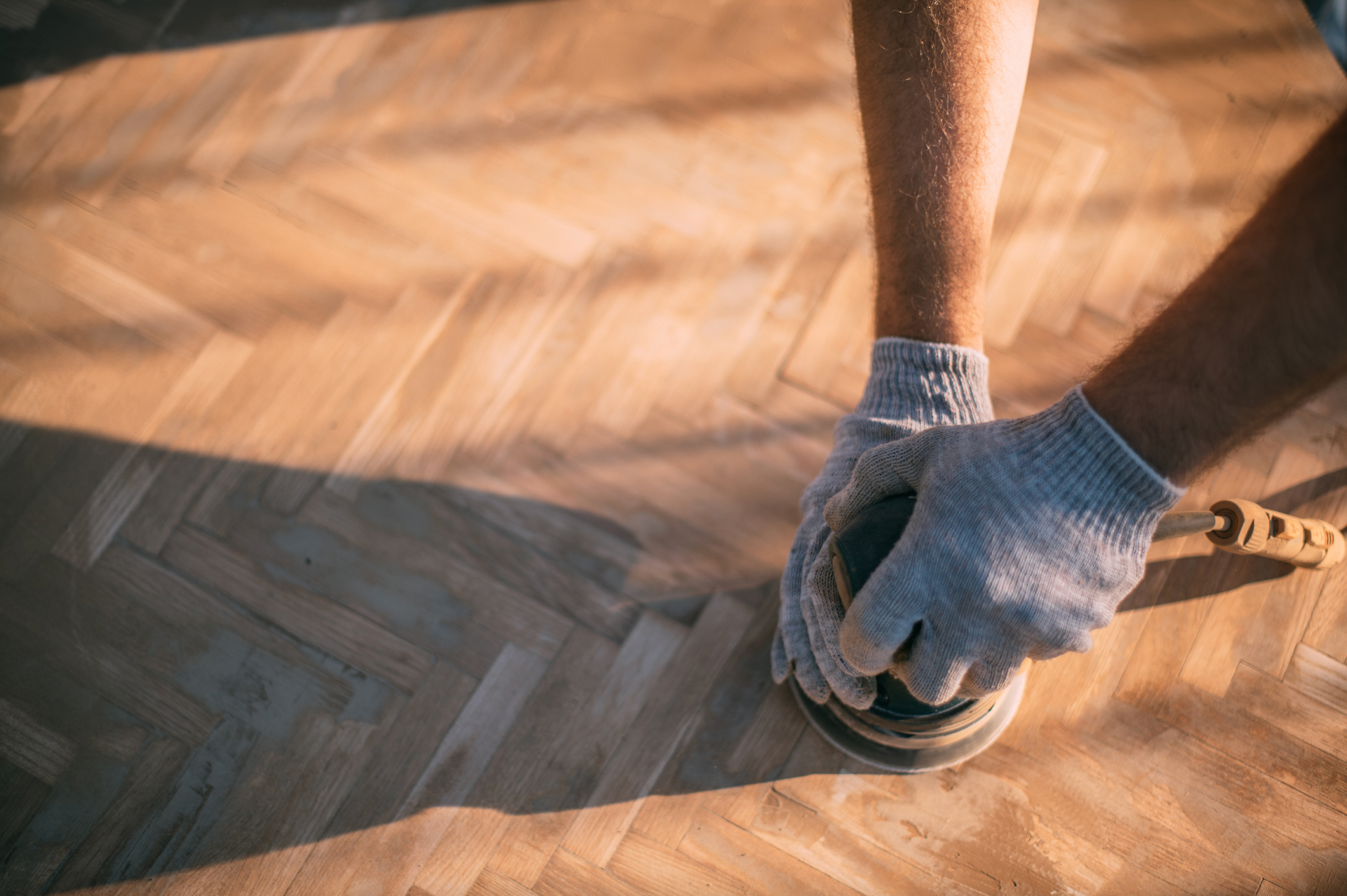 A person is sanding a wooden floor with a sander.