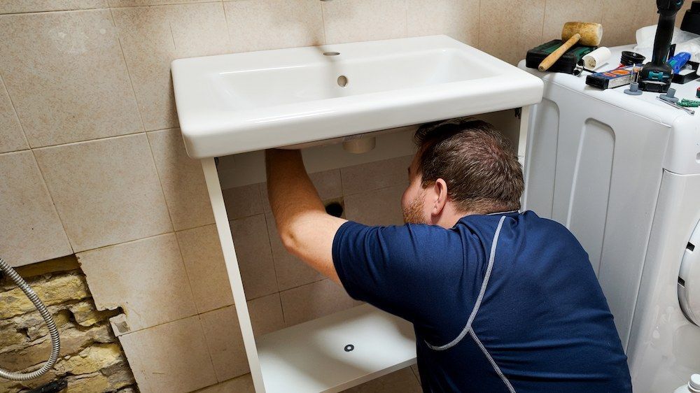 Man Installing a White Pipe of Sink in a Bathroom — David Lewis Solahart in Murwillumbah, NSW