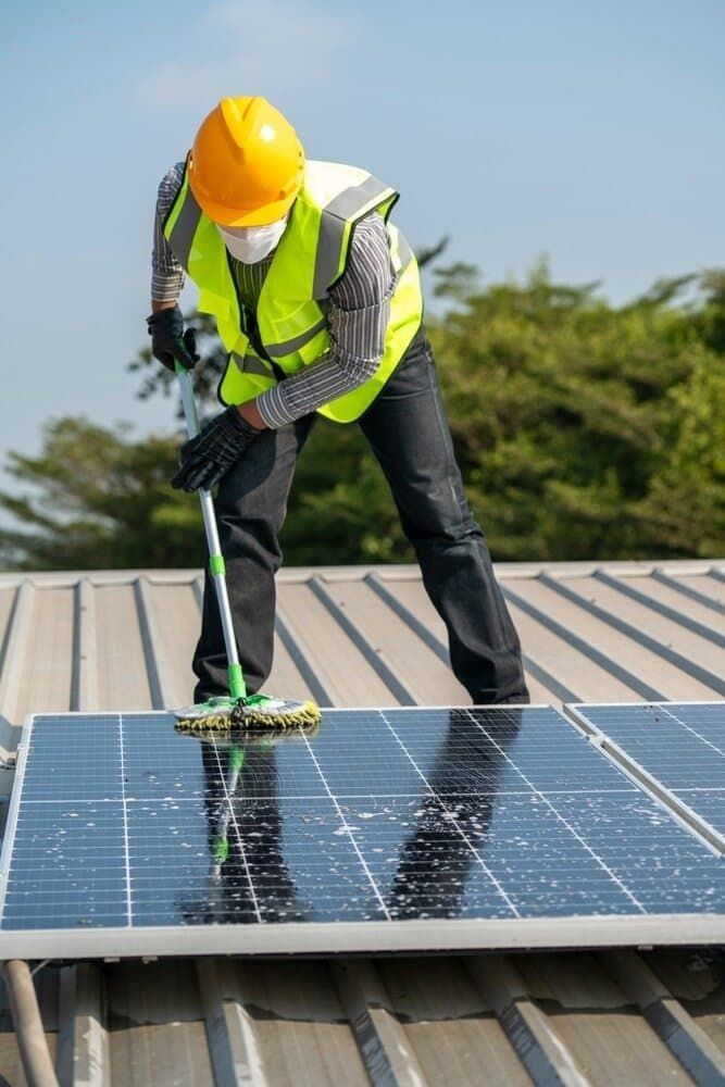 A Man Is Cleaning Solar Panels On The Roof Of A Building — David Lewis Solahart in Tenterfield, NSW