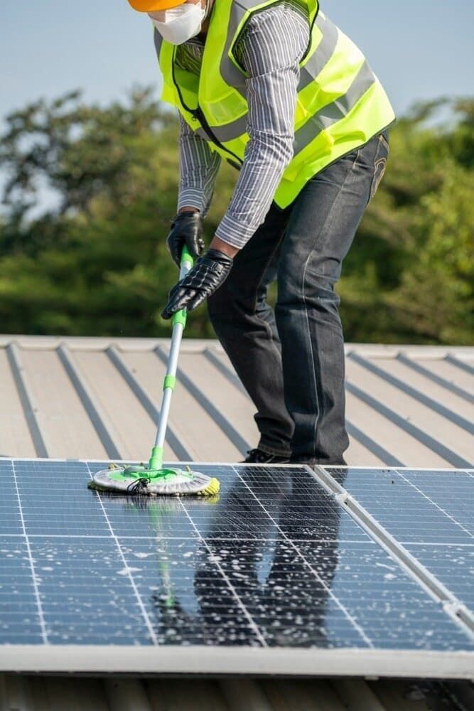 A Man Is Cleaning Solar Panels On A Roof With A Mop — David Lewis Solahart in Tenterfield, NSW