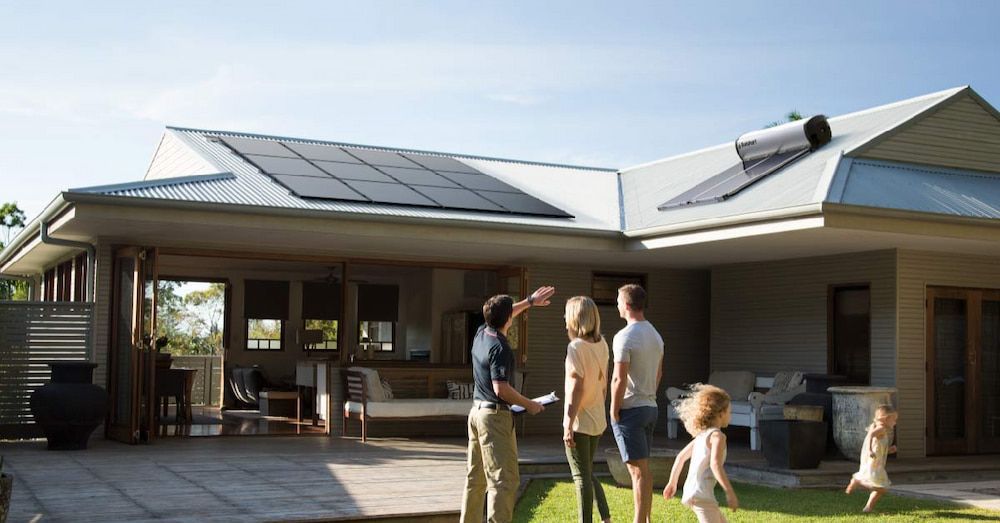 A Family Is Standing In Front Of A House With Solar Panels On The Roof — David Lewis Solahart in Goonellabah, NSW