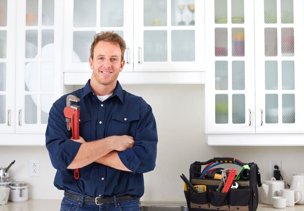A Plumber Is Standing In A Kitchen Holding A Wrench — Solahart In Goonellabah, NSW