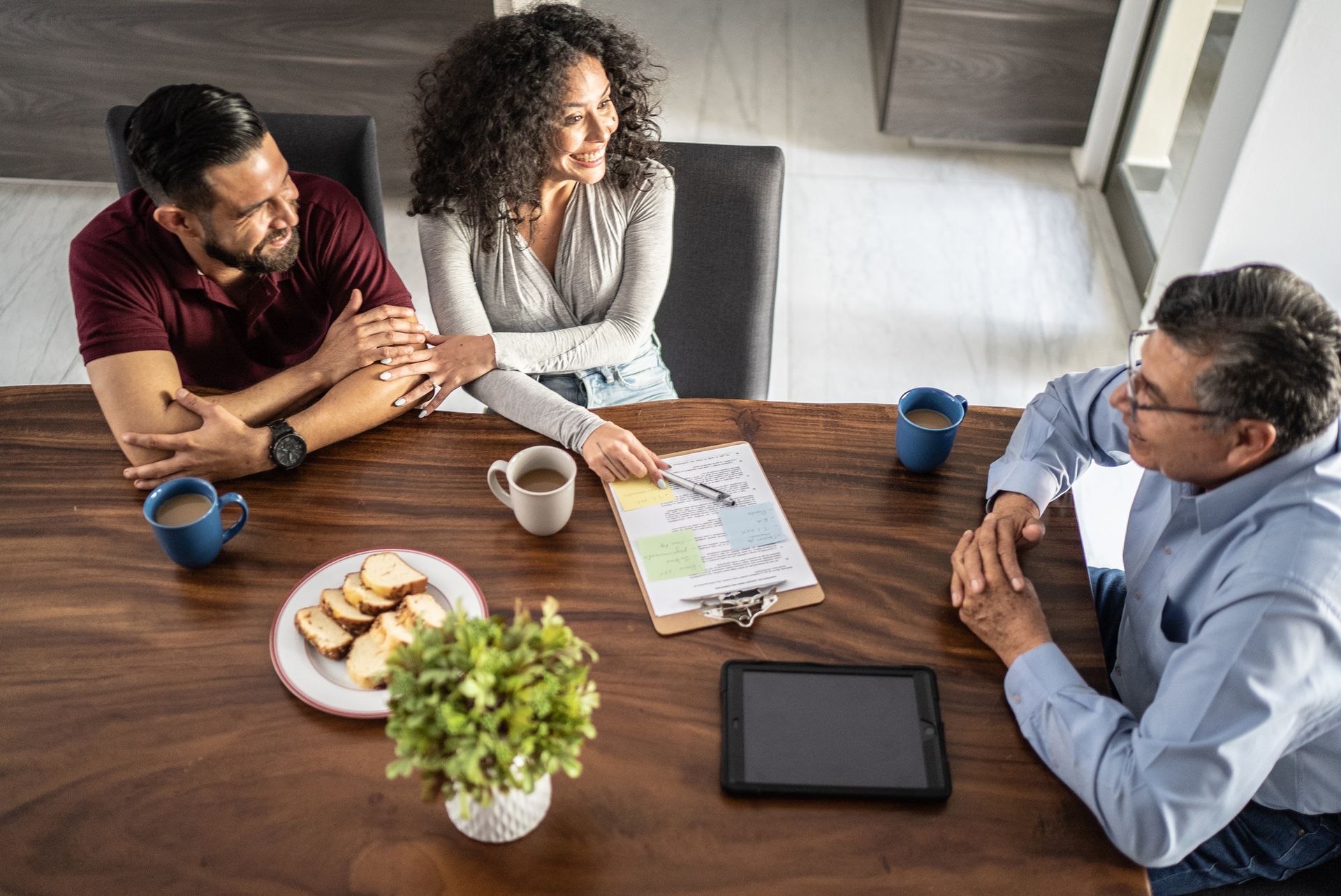 A couple consults with a man at a wooden table. The woman points to a document.