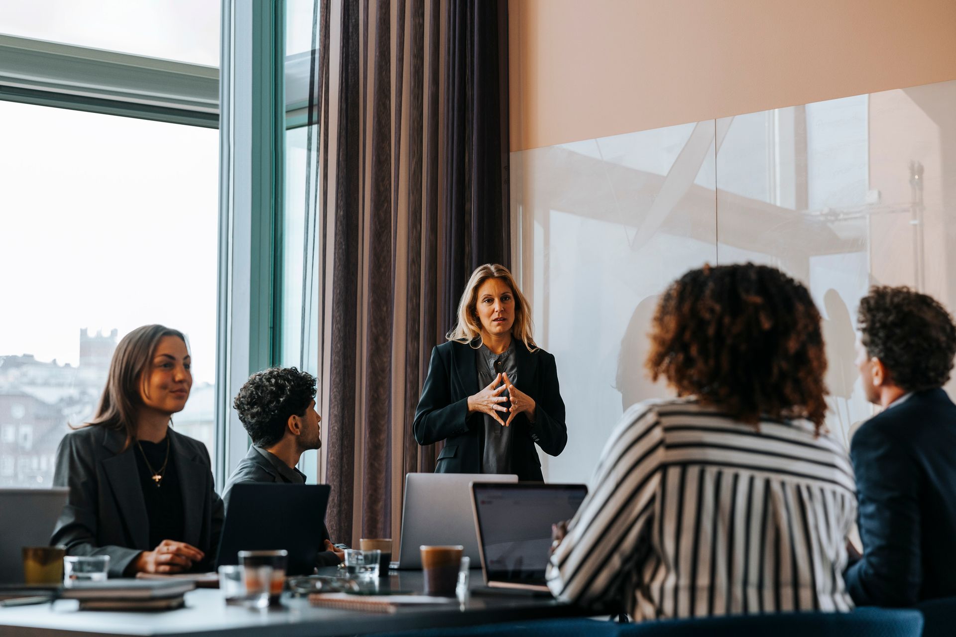Businesswoman giving a presentation to a group seated around a conference table, in a modern office.