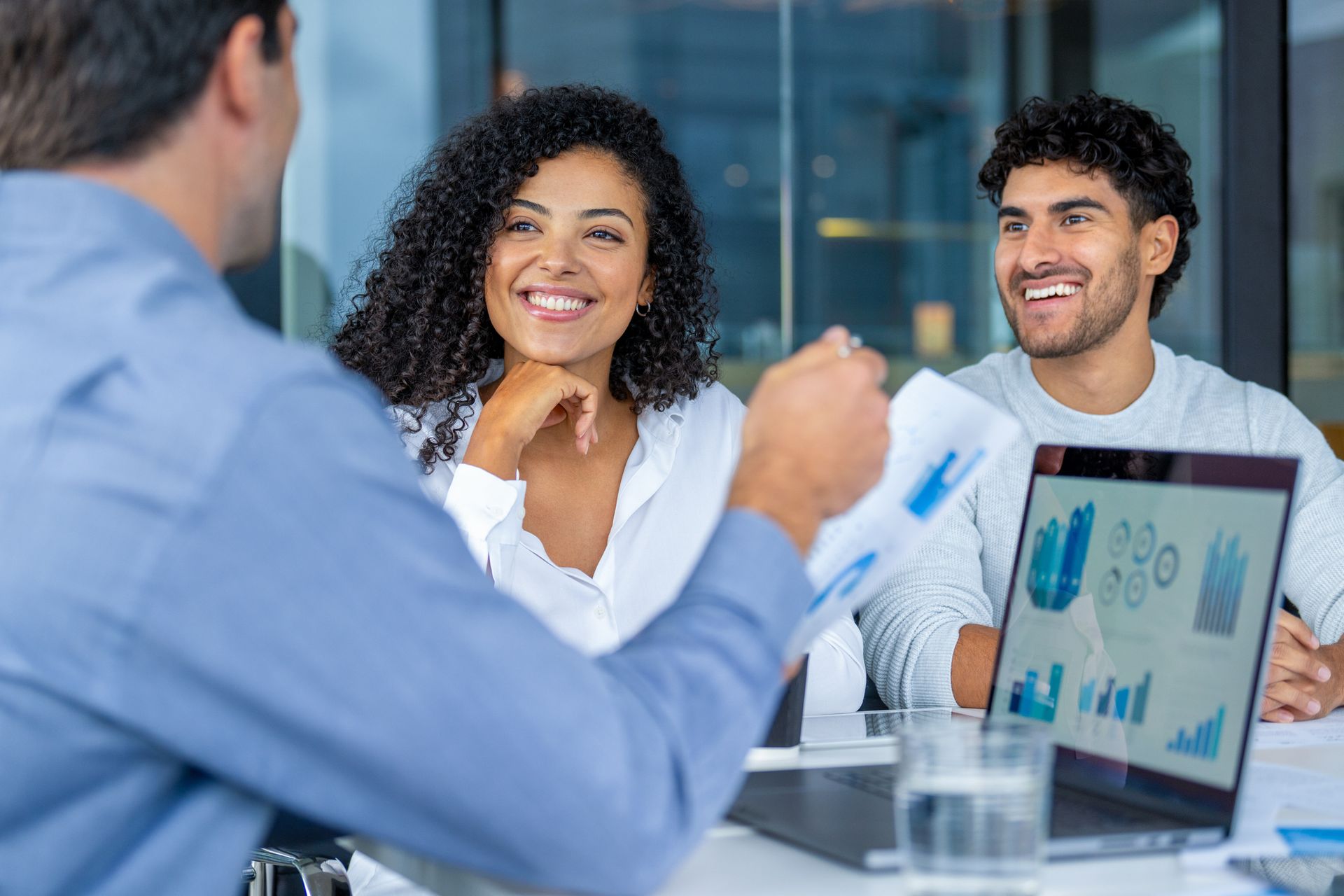 A financial advisor reviews documents with a smiling couple at a table in an office.