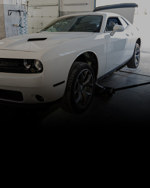 White Dodge Challenger lifted by a jack in a garage. | Lakeside Service Center