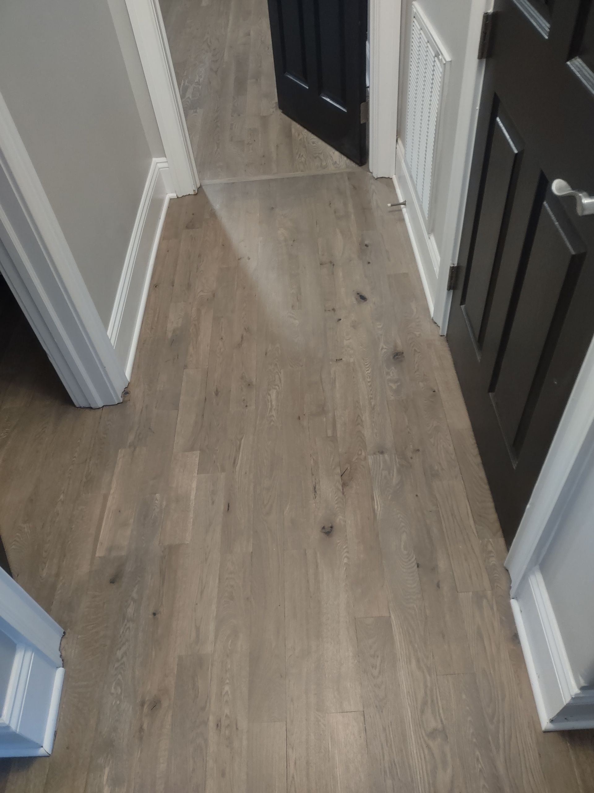 Wooden floor in hallway with grey walls and dark doors.