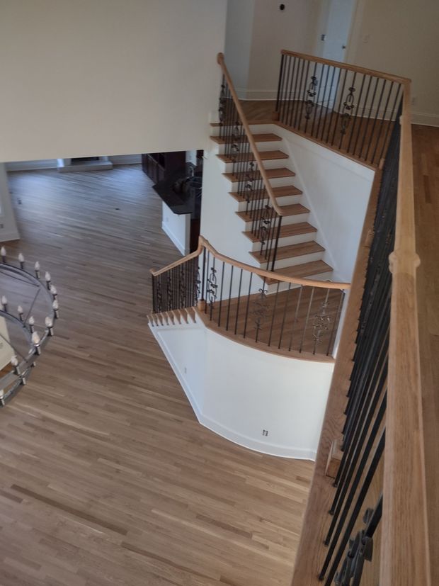 Wooden staircase with black railings, seen from above. Oak floors, white walls.
