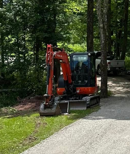 Orange excavator parked next to a gravel road in a wooded area.