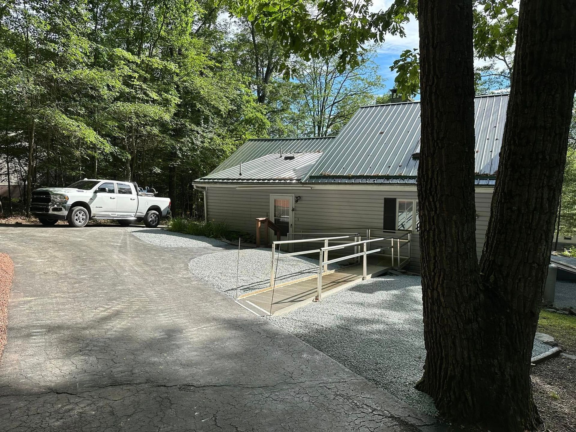 A white pickup truck parked on gravel driveway next to a small building with a ramp and metal roof.