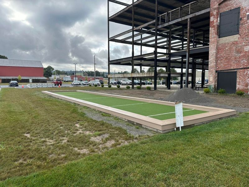 Bocce ball court with artificial turf, bordered by light wood, next to a building under construction.