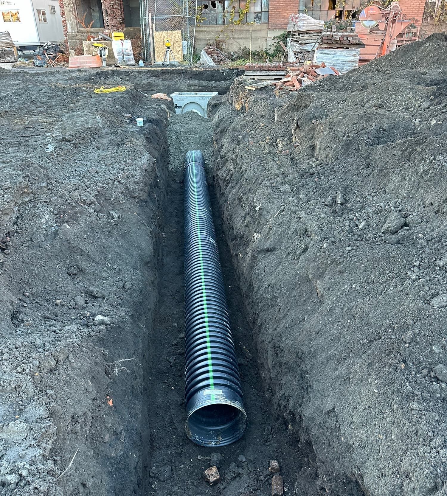 Black corrugated drainage pipe in a deep trench. Construction site.