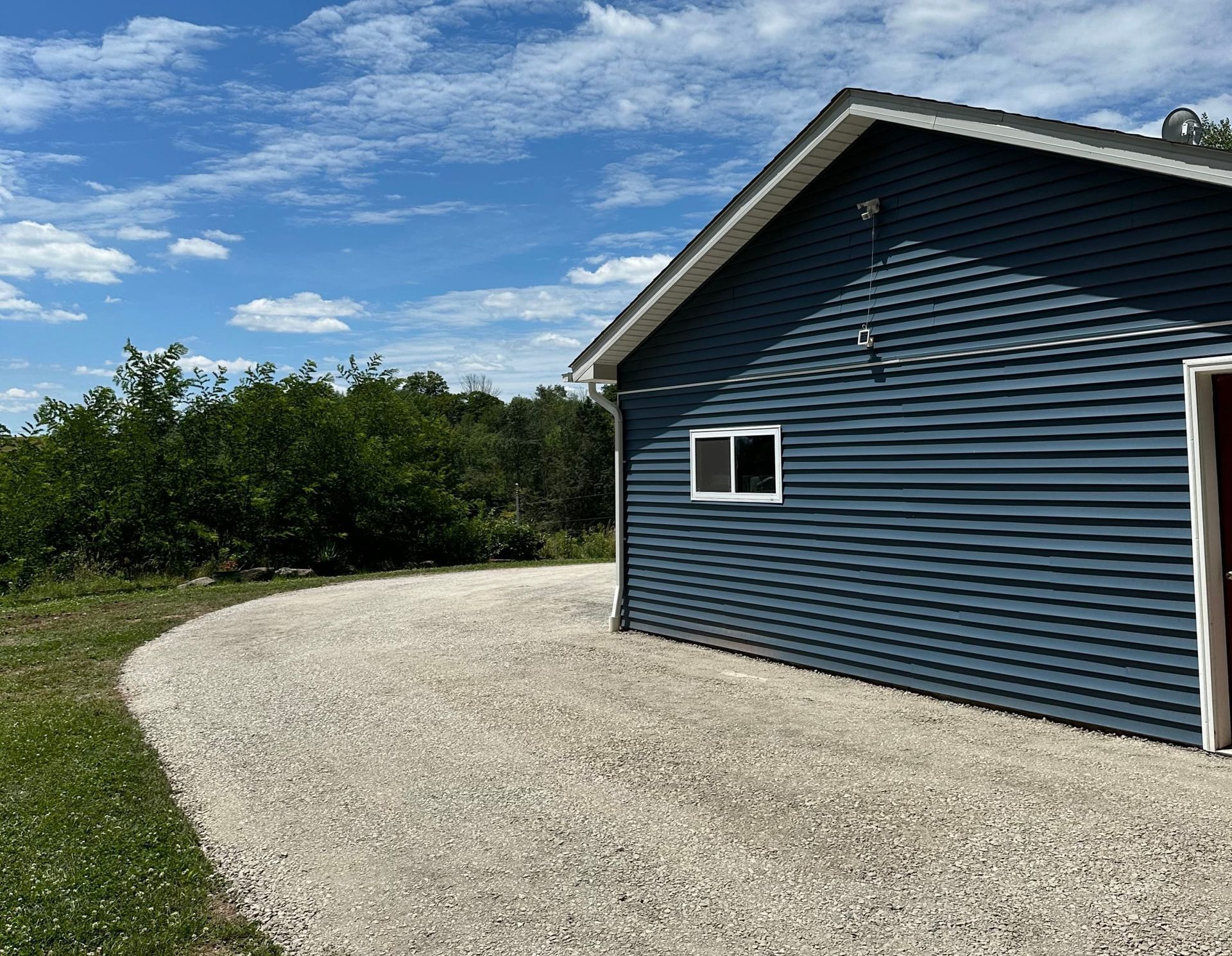 Blue building with gravel driveway under a partly cloudy sky.