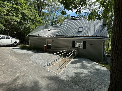 Building with ramp entrance; gray siding, metal roof, gravel parking, white truck on left.